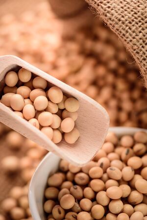 closeup is some soybeans in ceramic bowl with wooden spoon on sack backgroundの写真素材