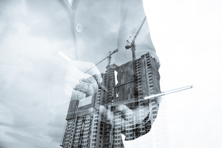 Double exposure of success businessman using digital tablet with Construction site with crane and buildingの写真素材