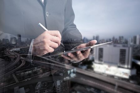 Double exposure of success businessman using digital tablet with city landscape backgroundの写真素材
