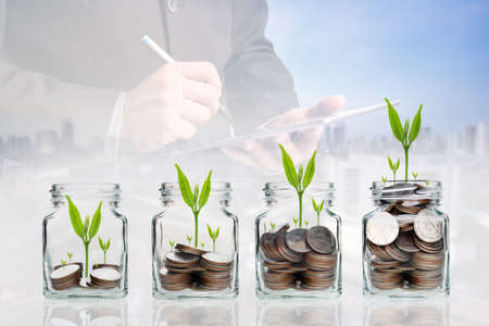 Double exposure of success businessman using digital tablet with coins with seed in clear bottle,Business investment growth concept,saving concept on city landscape backgroundの写真素材