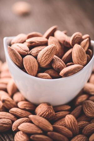 almonds in a white ceramic bowl on grained wood background,vintage tone