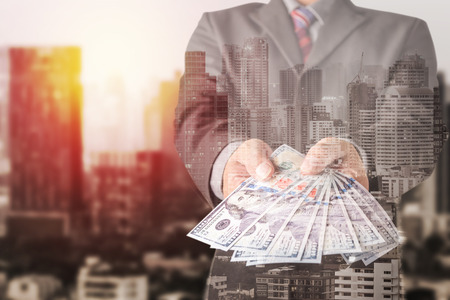 Double exposure of Businessman with money in hand with cityscape blurred building background, US...