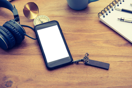 Top view of smartphone with white screen and gadgets on a wooden table background