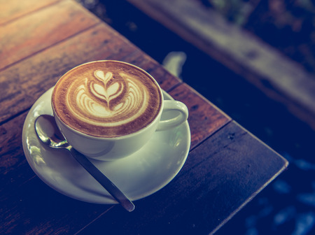 A Cup of hot latte art coffee on wooden table vintage tone styleの写真素材