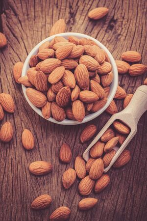 almonds in a white ceramic bowl on grained wood backgroundの写真素材