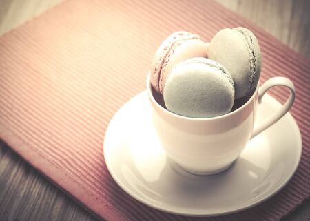 A lot of french colorful macarons on a woody floor,macarons in a cup ; vintage filter styleの写真素材