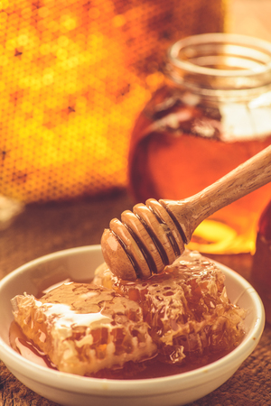 Honey  with honeycomb in white ceramic bowl and wooden drizzlerの写真素材