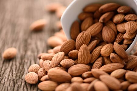 almonds in a white ceramic bowl on grained wood backgroundの写真素材