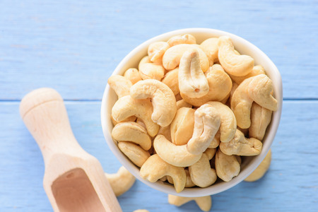 raw cashew nuts in white ceramic bowl on blue wood tableの写真素材
