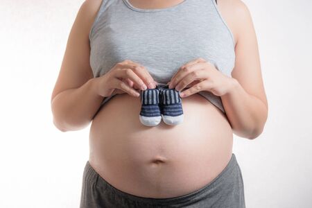 Pregnant woman holding small baby shoes on white background