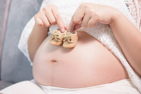 Pregnant woman holding small baby shoes relaxing at homeの写真素材
