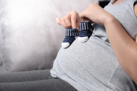 Pregnant woman holding small baby shoes on her bellyの写真素材