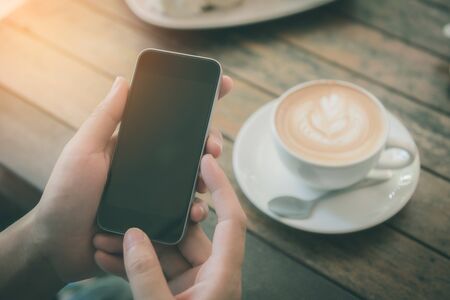 woman hand play smart phone with a cup of latte art coffee on the wood table.