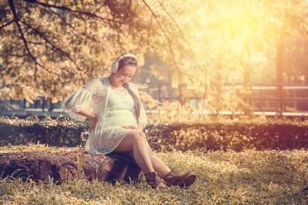 happy pregnant woman listening to a music at park.の写真素材
