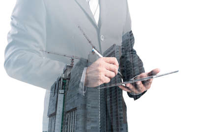 Double exposure of success businessman using digital tablet with Construction site with crane and building,business backgroundの写真素材