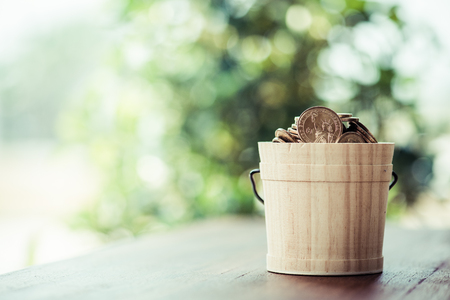 one dollar coin In a wooden bucket with green bokeh background.save and investment concept.の写真素材