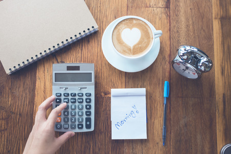 cup of Coffee latte art Heart shape with office tools on table,hand using calculator