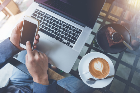 businessman working from home using smart phone and notebook computer, man's hands using smart phone in interior, man at his workplace using technologyの写真素材