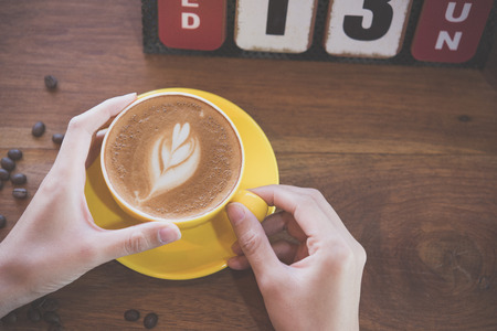 Coffee Latte art.Female hands holding a cup of coffee on wooden table in coffee shop.の写真素材