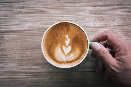 Man Hand holding Cup of coffee Latte art  on wooden table, top view,a cup of green pastel.の写真素材