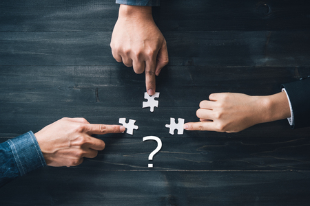 Teamwork concept using white puzzle pieces being fitted together by three male and female hands in a...