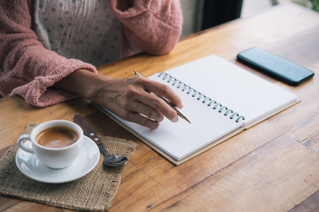 woman's hand writing on paper with cup of coffee espresso.の写真素材