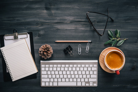 dark wood office desk table with blank notebook, supplies and coffee cup. Top view with copy space....