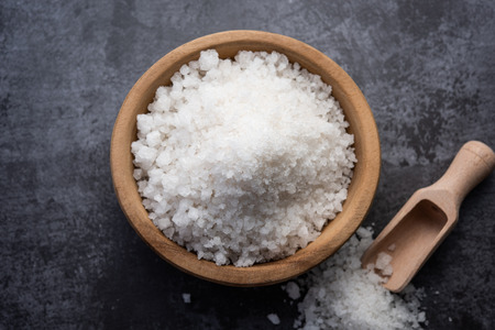 Salt in wooden bowl on stone table. Salt top view. Sea salt on dark background.