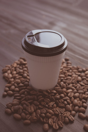 Disposable cup of coffee and coffee beans over dark wood background with space for your textの写真素材