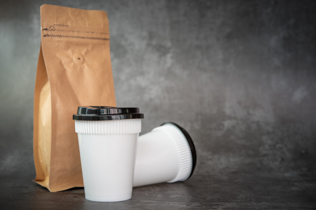 Disposable cup of coffee and coffee beans in paper bag over Cement Loft background with space for your textの写真素材
