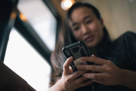 Happy smiling Asian woman holds mobile phone, close up focus on female hands and device. Customer buying goods via internet, friends chatting online, generation addicted with gadgets conceptの写真素材