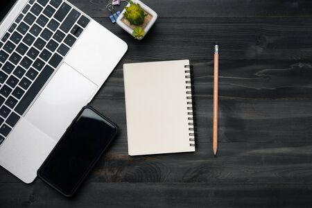 Modern dark wood office desk table with laptop, smartphone and other supplies. Blank notebook page for input the text in the middle. Top view, flat lay.の写真素材