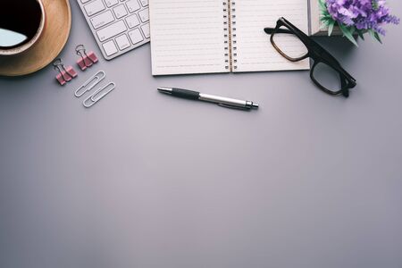 Flat lay, top view office table desk. Workspace with keyboard, office supplies, pencil, green leaf, and coffee cup on gray background.の写真素材