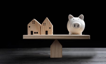 Home loans market. Model house and piggy bank balancing on a seesawの写真素材