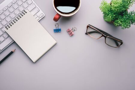Flat lay, top view office table desk. Workspace with keyboard, office supplies, pencil, green leaf, and coffee cup on gray background.の写真素材