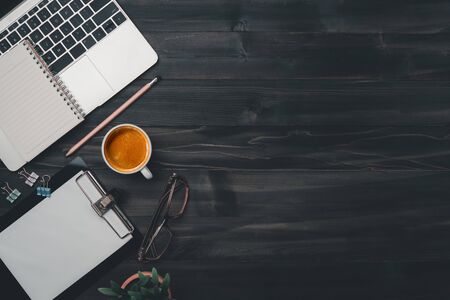 Modern dark wood office desk table with laptop, smartphone and other supplies with cup of coffee. Blank notebook page for input the text in the middle. Top view, flat lay.の写真素材