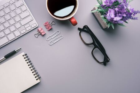 Flat lay, top view office table desk. Workspace with keyboard, office supplies, pencil, green leaf, and coffee cup on gray background.の写真素材