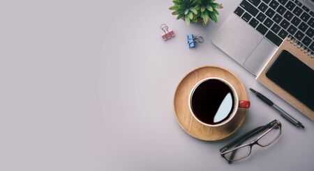 Flat lay, top view office table desk. Workspace with keyboard, office supplies, pencil, green leaf, and coffee cup on gray background.の写真素材