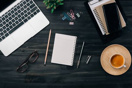 Modern dark wood office desk table with laptop, smartphone and other supplies with cup of coffee. Blank notebook page for input the text in the middle. Top view, flat lay.の写真素材