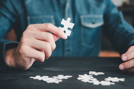 Closeup hand of businessman connecting jigsaw puzzle with darkwood background, Business solutions, success and strategy conceptの写真素材