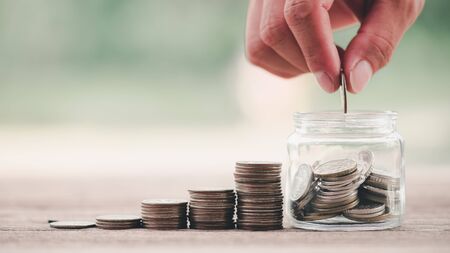 Close up of stacking coins with hand putting Money in the jar on wooden table .The concept of saving money for the future. Financial money concepts and savings.investment.の写真素材