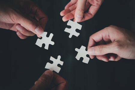 Teamwork concept using white puzzle pieces being fitted together by three male and female hands in a challenge, brainstorming and solution concept.の写真素材