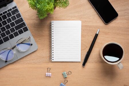 Wooden office desk table with blank notebook, laptop computer, cup of black coffee and supplies. Top view with copy space, flat lay.の写真素材