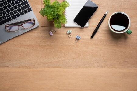 wooden office desk table with smartphone with blank mock up screen, laptop computer, cup of black coffee and supplies. Top view with copy space, flat lay.の写真素材