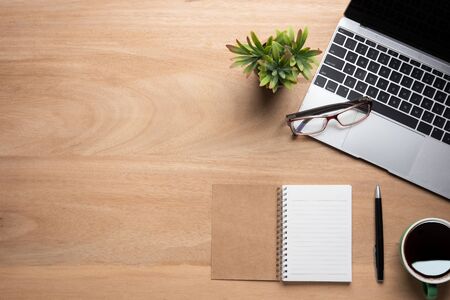 Wooden office desk table with blank notebook, laptop computer, cup of black coffee and supplies. Top view with copy space, flat lay.の写真素材
