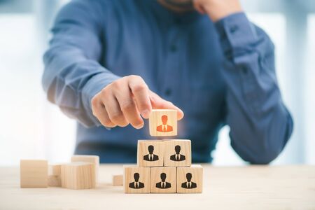Midsection of businesswoman stacking wooden team blocks at table.Human resources and corporate hierarchy concept, recruiter complete team by one leader person represented by icon.の写真素材