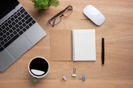 Wooden office desk table with blank notebook, laptop computer, cup of black coffee and supplies. Top view with copy space, flat lay.の写真素材