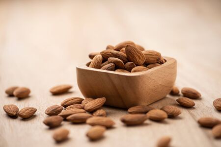 Almonds in wood bowl on light wood table. Almond concept with copyspace.の写真素材