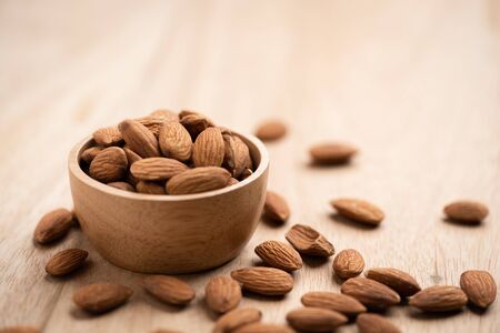 Almonds in wood bowl on light wood table. Almond concept with copyspace.の写真素材