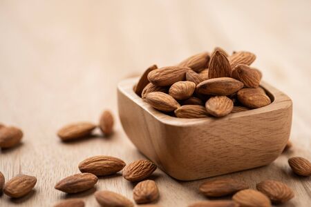 Almonds in wood bowl on light wood table. Almond concept with copyspace.の写真素材